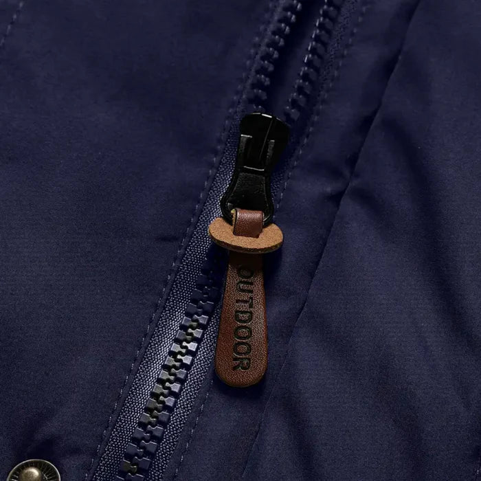 Nahaufnahme eines dunkelblauen Outdoorjacke-Reißverschlusses mit braunem Lederanhänger.
