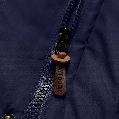 Nahaufnahme eines dunkelblauen Outdoorjacke-Reißverschlusses mit braunem Lederanhänger.